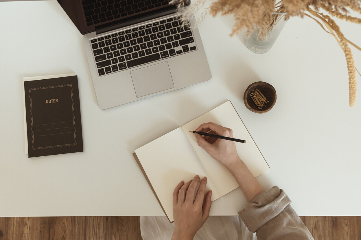 Man Writing on Notebook with Laptop on Table Top View